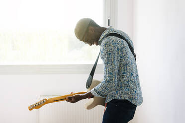 Lächelnder junger Popmusiker spielt Gitarre am Fenster - JCMF00746