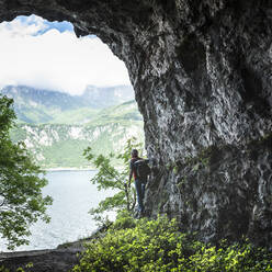 Älterer männlicher Wanderer steht an einer Felsformation und blickt vom Höhleneingang auf den Comer See - MCVF00396