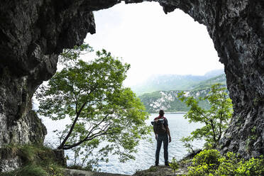 Male hiker looking at Lake Como against sky from cave entrance - MCVF00399