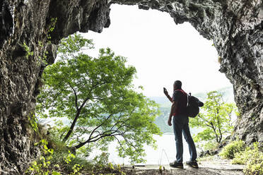 Mature male explorer photographing Lake Como from cave entrance - MCVF00402