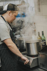 Young male chef cooking food in pot at restaurant kitchen - PSIF00388