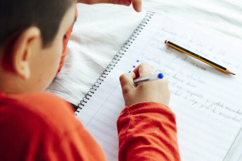 Young boy writing in book with pen during homeschooling - JCMF00761