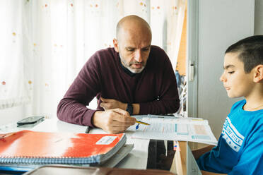 Selbstbewusster Vater unterrichtet seinen Sohn am Schreibtisch sitzend während des Homeschoolings - JCMF00762