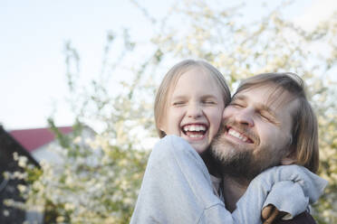 Nahaufnahme eines fröhlichen Mädchens, das seinen Vater im Hinterhof umarmt - EYAF01072