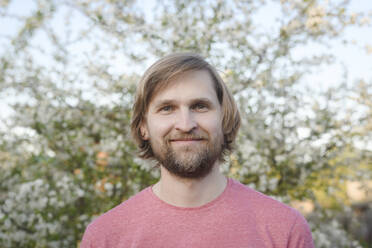 Close-up portrait of smiling bearded man against tree at back yard - EYAF01075