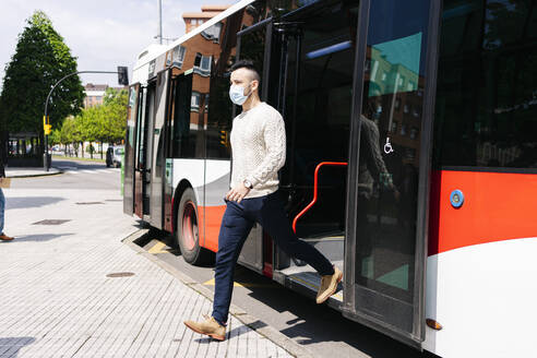 Junger Mann mit Schutzmaske beim Aussteigen aus einem öffentlichen Bus, Spanien - DGOF01008