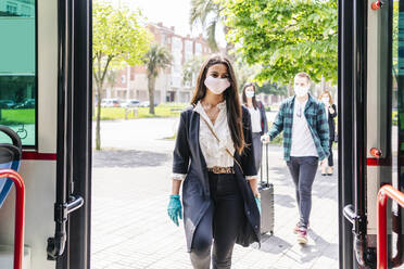 Portrait of young woman wearing protective mask and gloves getting into bus, Spain - DGOF01009