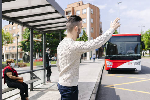 Mann mit Schutzmaske steht an einer Bushaltestelle und ruft ein Taxi, Spanien - DGOF01012