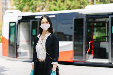 Portrait of young woman wearing protective mask and gloves waiting at bus stop, Spain - DGOF01018