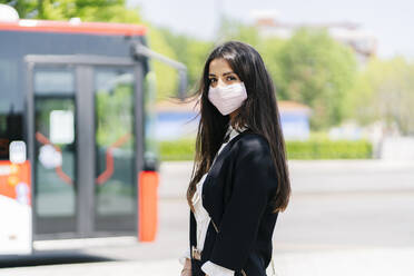 Portrait of young woman wearing protective mask waiting at bus stop, Spain - DGOF01019