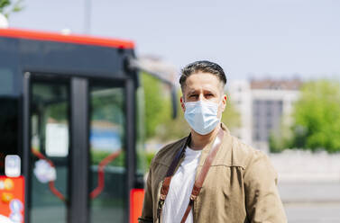 Porträt eines Mannes mit Schutzmaske, der an einer Bushaltestelle wartet, Spanien - DGOF01028