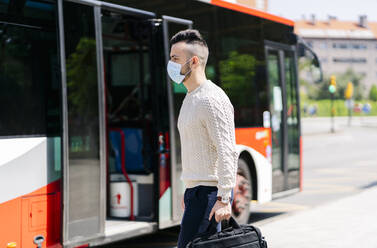 Young man wearing protective mask walking in front of public bus, Spain - DGOF01031