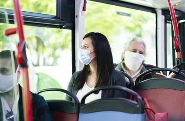 Frau mit Schutzmaske sitzt im Bus und schaut aus dem Fenster, Spanien - DGOF01034