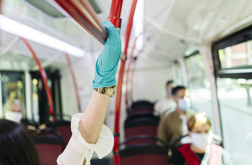 Junge Frau trägt Schutzhandschuhe in einem öffentlichen Bus, Spanien - DGOF01036