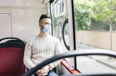 Porträt eines jungen Mannes mit Schutzmaske, der in einem Linienbus sitzt und aus dem Fenster schaut, Spanien - DGOF01042