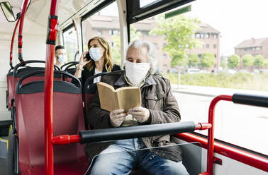 Älterer Mann mit Schutzmaske im öffentlichen Bus beim Lesen eines Buches, Spanien - DGOF01045