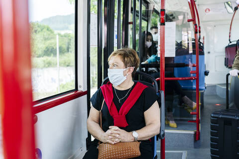 Porträt einer reifen Frau mit Schutzmaske in einem öffentlichen Bus, die aus dem Fenster schaut, Spanien, lizenzfreies Stockfoto