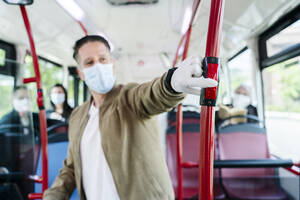 Man wearing protective mask and gloves in public bus pressing stop button, Spain - DGOF01063