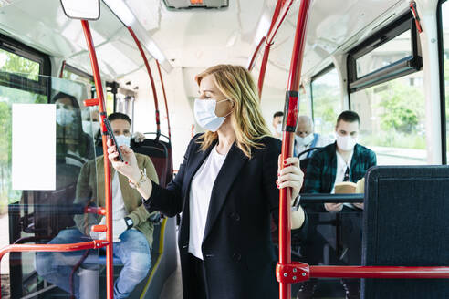 Geschäftsfrau mit Schutzmaske in einem öffentlichen Bus, die auf ihr Handy schaut, Spanien - DGOF01077