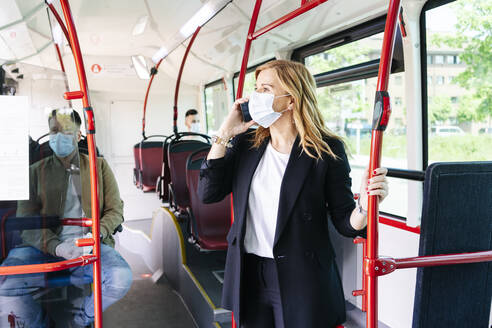 Businesswoman on the phone wearing protective mask in public bus, Spain - DGOF01078