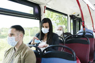 Frau mit Schutzmaske im öffentlichen Bus beim Desinfizieren ihrer Hände, Spanien - DGOF01079