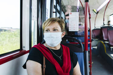 Porträt einer reifen Frau mit Schutzmaske in einem öffentlichen Bus, die aus dem Fenster schaut, Spanien - DGOF01080