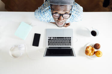 Porträt eines jungen Mannes am Schreibtisch mit Laptop im Heimbüro - JCMF00769