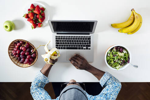 Mann arbeitet beim Essen am Schreibtisch im Home Office - JCMF00775