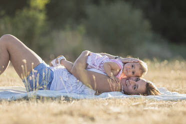 Porträt einer lächelnden Frau und ihrer Tochter auf einer Picknickdecke auf einer Wiese an einem sonnigen Tag - SNF00230