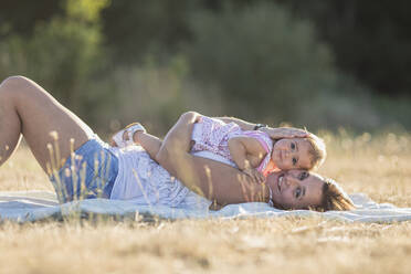 Portrait of smiling woman and daughter lying on picnic blanket on meadow during sunny day - SNF00230