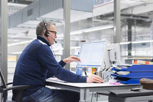 Mann mit Headset sitzt am Schreibtisch im Büro - DIGF11394