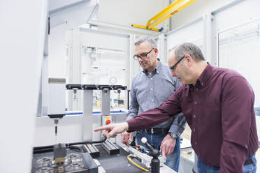 Two businessmen having a discussion at a machine in a factory - DIGF11409