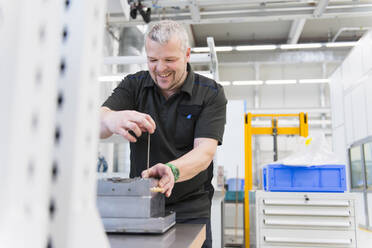 Lächelnder Mann bei der Arbeit an einer Werkbank in einer Fabrik - DIGF11417