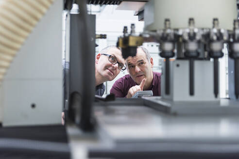 Zwei Geschäftsleute im Gespräch an einer Maschine in einer Fabrik - DIGF11419