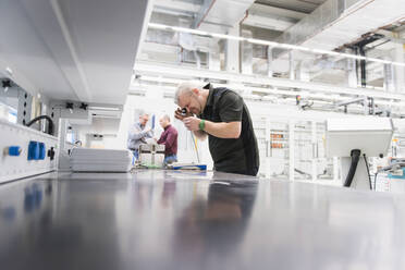 Mann prüft Produkt in einer Fabrik mit Kollegen im Hintergrund - DIGF11421