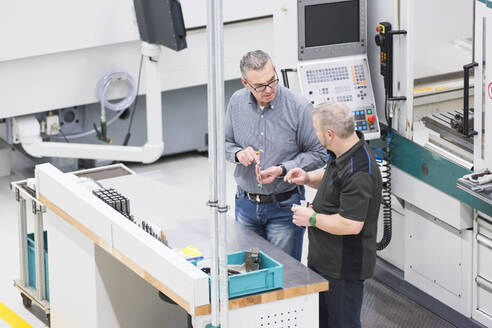 Zwei Männer unterhalten sich an einer Maschine in einer Fabrik - DIGF11437
