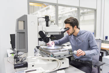 Mann schaut durch ein Mikroskop in einer Fabrik - DIGF11449