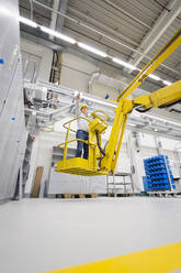 Man wearing hard hat standing on hoist in a factory - DIGF11487