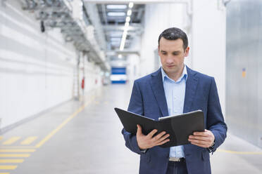 Businessman holding folder on factory corridor - DIGF11489