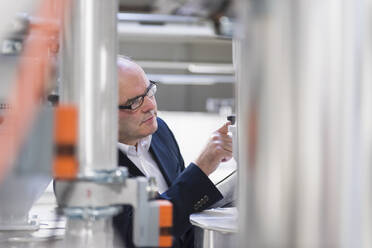 Businessman examining a machine in a factory - DIGF11506