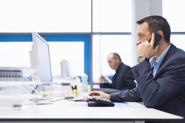 Businessman on the phone using computer in office - DIGF11524