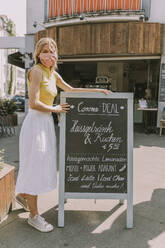 Cafe owner wearing face mask posting a board with Corona special offers - MFF05669