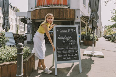 Cafe owner wearing face mask posting a board with Corona special offers - MFF05670