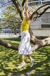 Portrait of happy woman hanging from a branch in a tree - MFF05702