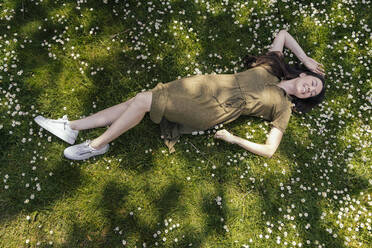 Frau genießt ihre Freizeit, während sie im Gras mit Gänseblümchen liegt - MFF05705