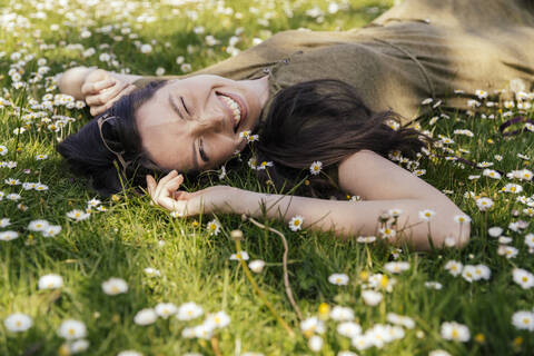 Happy woman enjoying her free time while lying on grass with daisies stock photo