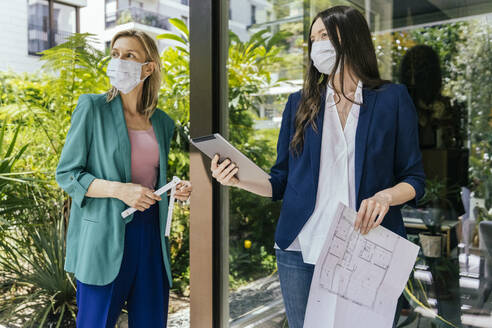 Zwei Immobilienmakler mit Gesichtsmasken bei der Inspektion des Außenbereichs eines Hauses - MFF05712