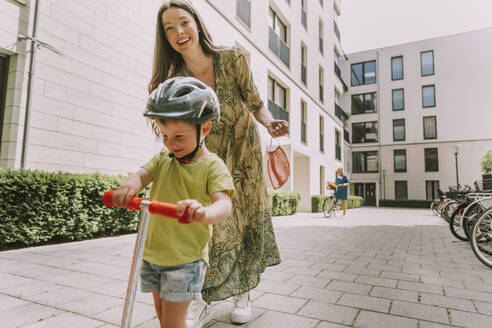 Lächelnde Mutter mit Gesichtsmaske und Sohn mit Motorroller in der Stadt - MFF05728