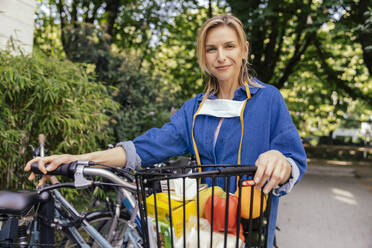 Portrait of confident woman with let down face mask and bicycle and groceries - MFF05732