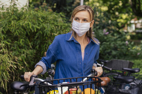 Frau mit Gesichtsmaske, die mit dem Fahrrad in der Stadt Lebensmittel einkaufte, lizenzfreies Stockfoto